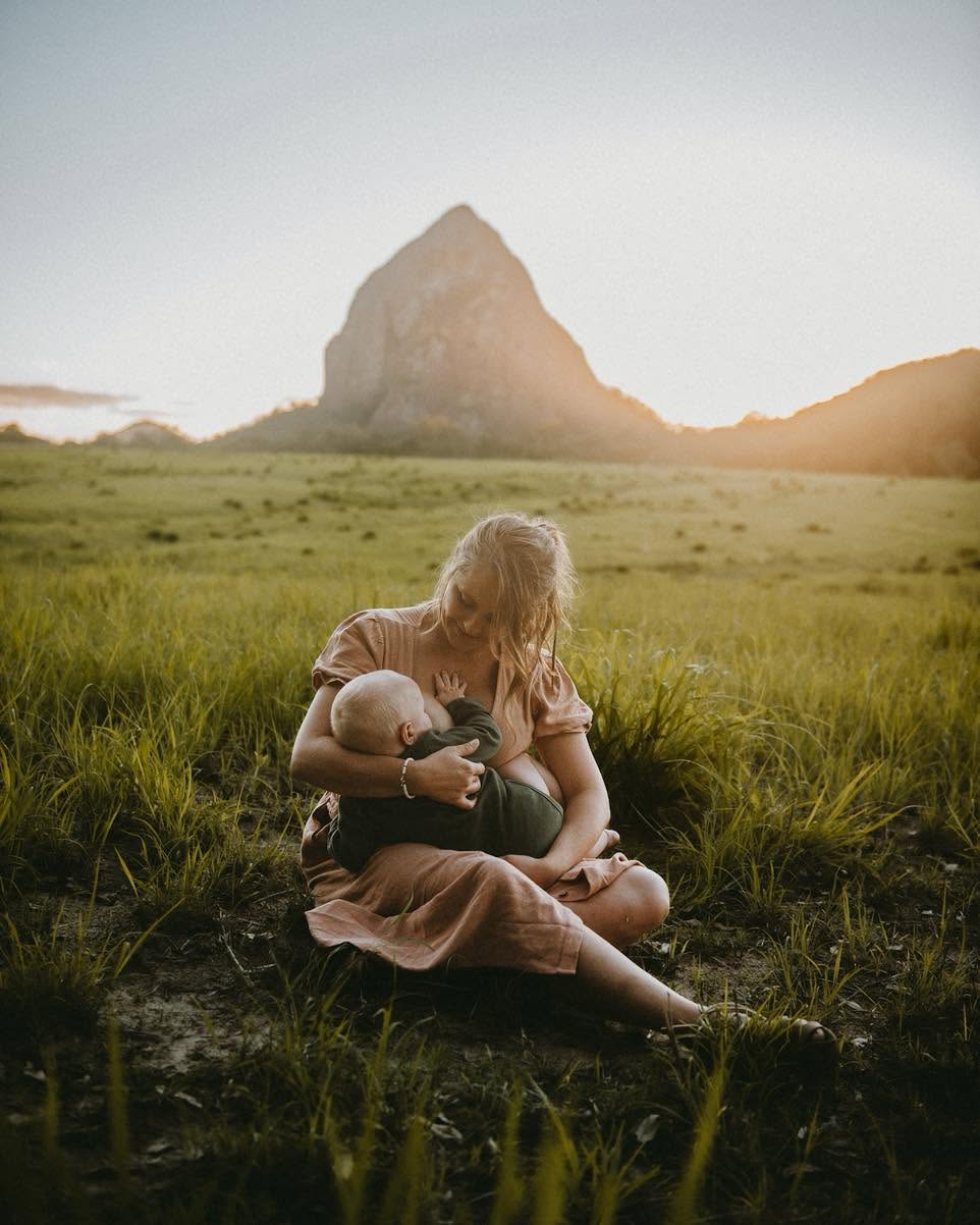 Mum feeding her baby in a field below the Glass House Mountains