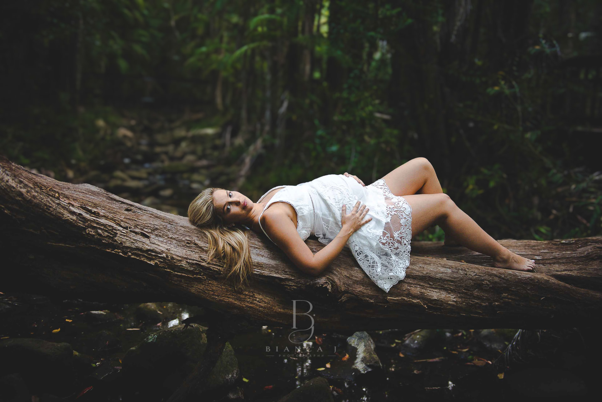 Mum-to-be in white lace lying on a log in the rainforest