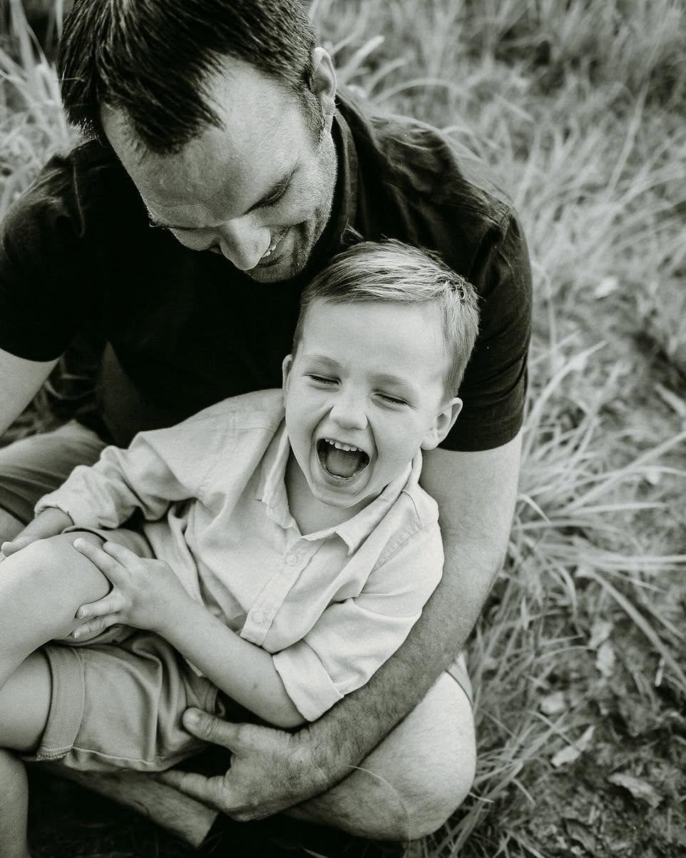 Dad tickling his laughing son, black and white