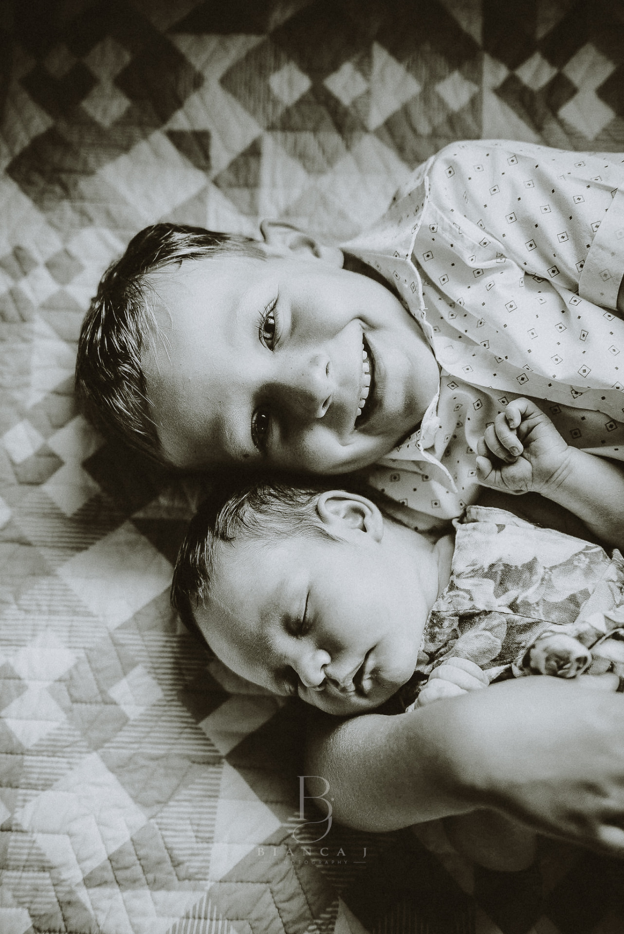 Big brother grinning beside his sleeping newborn sibling
