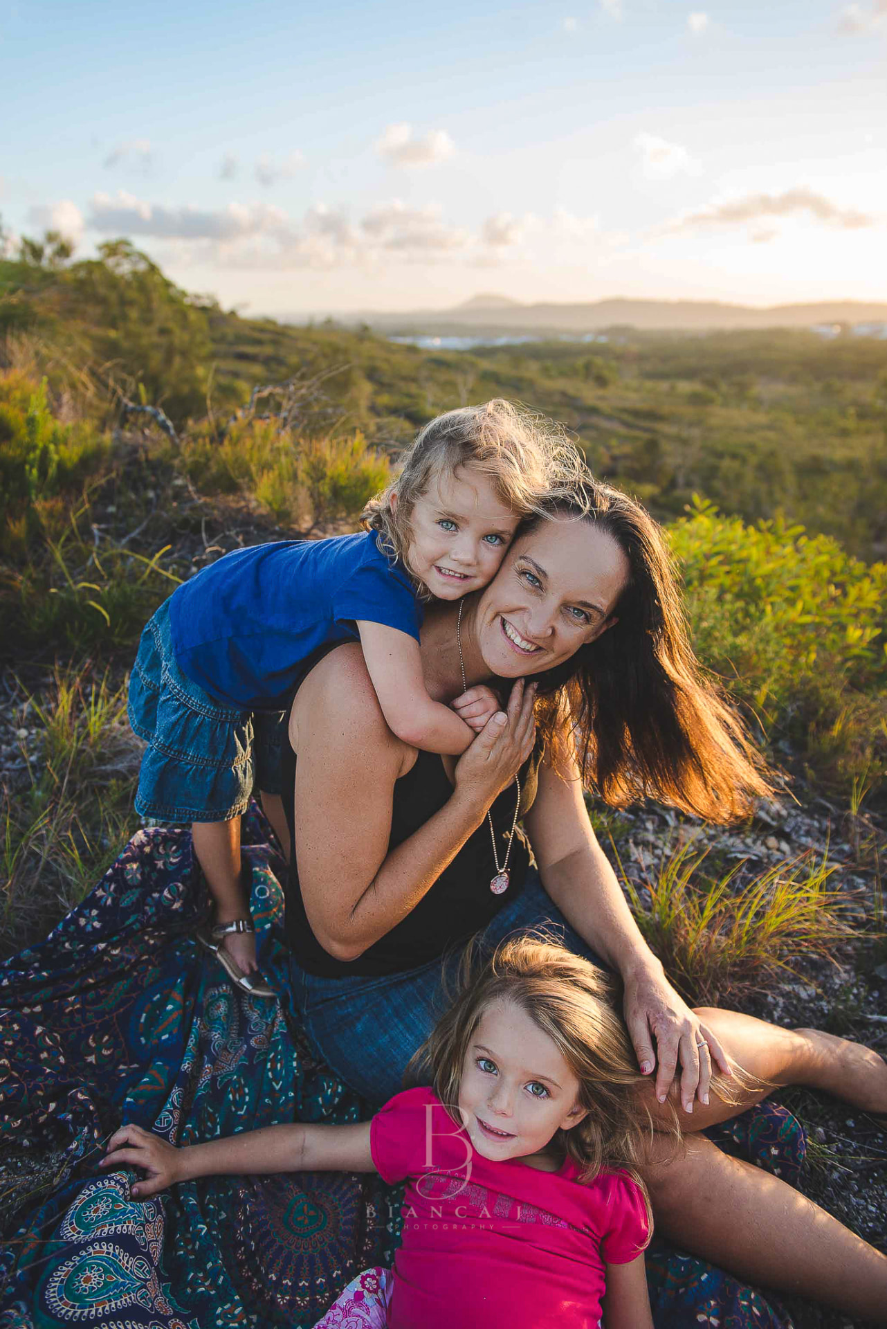 Mum and her two girls on a hilltop at sunset